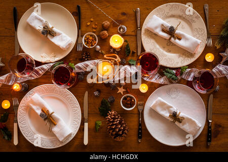 Christmas table setting for family dinner at a cosy rustic table with candles and decorations. Top view. Stock Photo