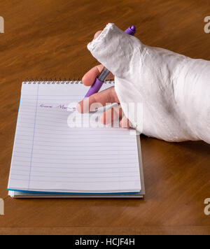 Person wearing an arm cast after breaking his wrist trying to write a note on a piece of paper Stock Photo