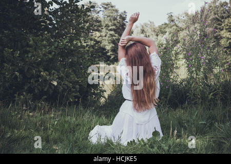 Haired young woman with long hair sitting on the grass back to Stock Photo