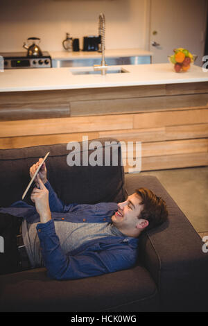 Smiling man lying on sofa using digital tablet in living room Stock Photo