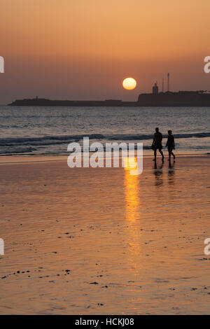 Romantic couple walking on a beach with a sun hiding Stock Photo