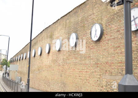 Long row of international clocks on a brick wall Stock Photo