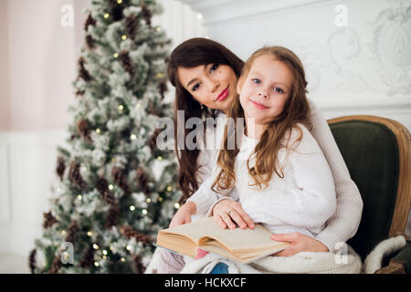 Girl and her mom reading book at Christmas Stock Photo