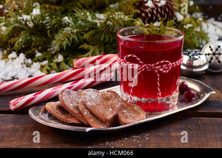 Glass of cranberry fruit drink and ginger cookies on metal plate over old wooden table. Stock Photo