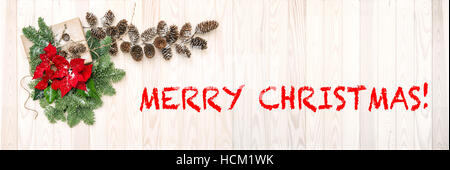 Pine branches with red poinsettia flower decoration on wooden background. Brush painted text Merry Christmas! Stock Photo