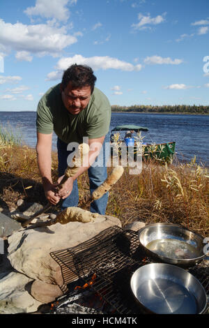 An indigenous man making bannock on a stick, a native North American food similar to bread, in Northern Ontario, Canada. Stock Photo