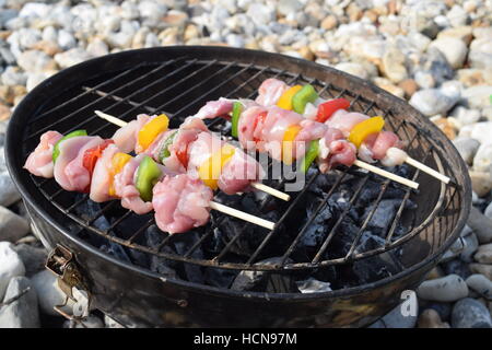 Mini outdoor barbecue on the beach with chicken skewers and vegetables Stock Photo