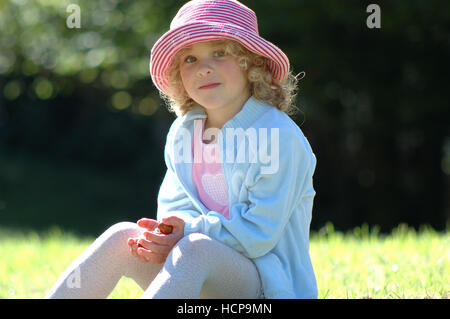 5-year-old laughing girl, backlit, wearing a hat, sitting Stock Photo