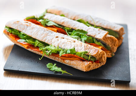 Healthy fresh crusty baguette submarine sandwich with salami, cheese and rucola. Selective focus Stock Photo