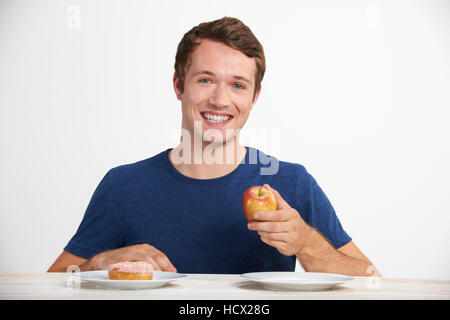 Young Man Choosing Between Doughnut And Cake For Snack Stock Photo