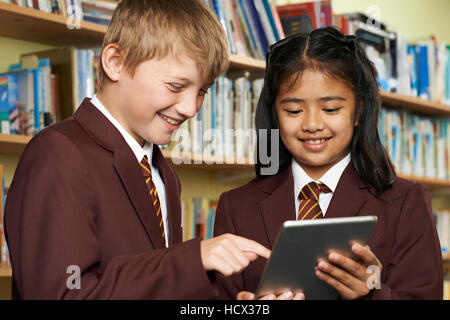 Pupils Wearing School Uniform Using Digital Tablet In Library Stock Photo