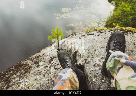 Male feet in camouflage pants and black rough shoes. Travel lifestyle background. Vintage tonal correction photo filter, old style Stock Photo