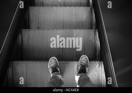 Male feet in canvas shoes stand on escalator stairs, black and white Stock Photo