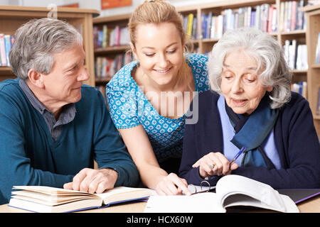 Mature Students Working With Teacher In Library Stock Photo