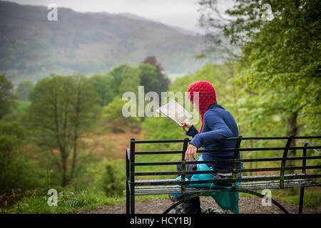 A woman rests on a bench while walking in The Lake District near Grasmere, Cumbria, UK Stock Photo