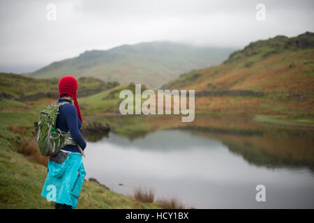 A woman looks out over Alcock Tarn near Grasmere, Lake District, Cumbria, UK Stock Photo