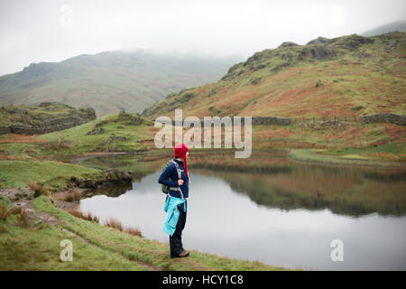 A woman looks out over Alcock Tarn near Grasmere, Lake District National Park, Cumbria, UK Stock Photo