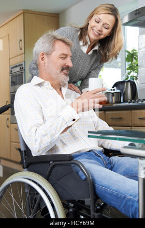 Woman Bringing Man In Wheelchair Hot Drink At Home Stock Photo