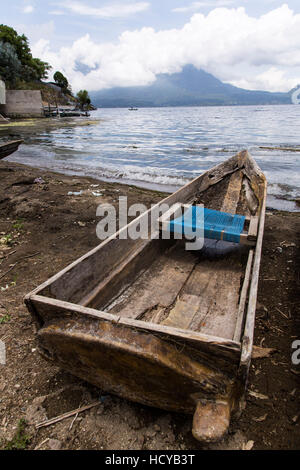 A cayuco or fishing boat on the shore of Lake  Atitilan at San Antonio Palopó, Guatemala with Lake Atitlan and the San Pedro Volcano in the clouds. Stock Photo