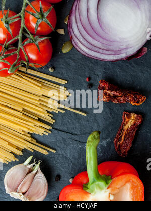 Pasta ingredients: pasta, avocado, arugula, tomatoes, garlic, peppers, sun-dried tomatoes  on black stone background with a copy space in the center Stock Photo