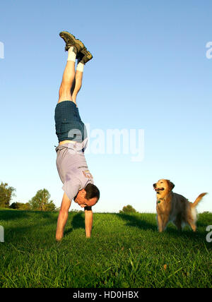 Photographer H. Mark Weidman doing a handstand in a green field with a Golden Retriever looking on. Stock Photo