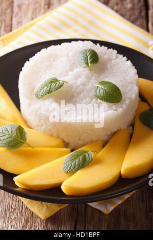 Glutinous rice with ripe mango close-up on a plate on the table. Vertical Stock Photo