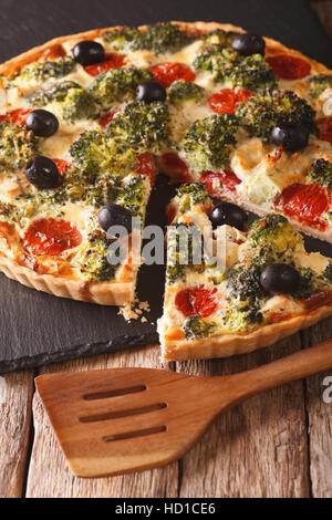 Savory food: sliced tart with chicken, broccoli, tomatoes and olives close-up on the table. vertical Stock Photo
