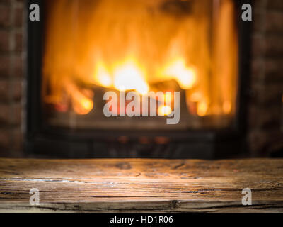 Old wooden table and fireplace with warm fire on the background. Stock Photo
