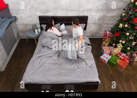Young couple preparing to sleep and wearing pajamas at home near Christmas tree with presents Stock Photo