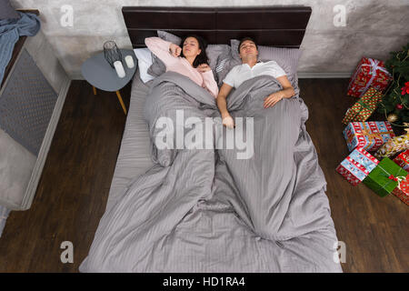 Young couple wake up wearing pajamas at home near Christmas tree with presents Stock Photo