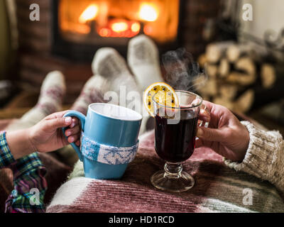 Warming and relaxing near fireplace. Mother and daughter with the cups of hot drink in front of fire. Stock Photo