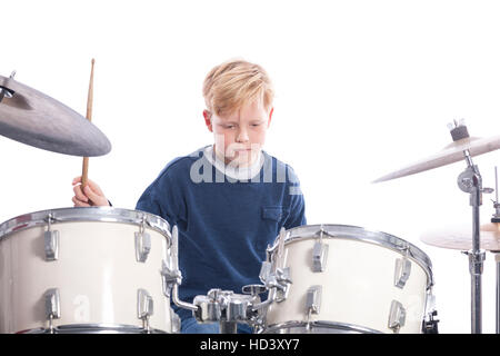 young blond boy drums behind drum kit against white background in studio Stock Photo