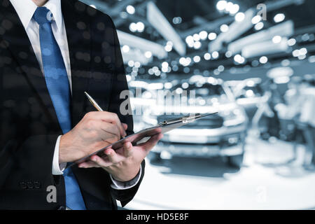 Double exposure of salesman hands holding trade booking with blurred background of new car displayed in showroom dealer, buying new car. Stock Photo