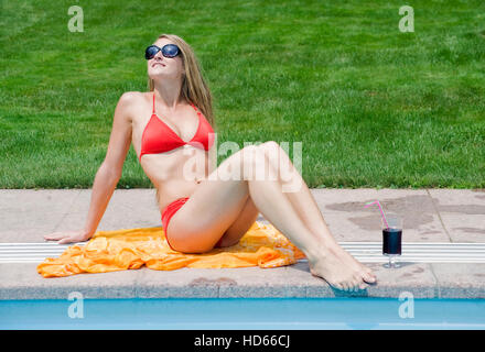 Young, attractive woman wearing a red bikini and sunbathing next to a swimming pool Stock Photo