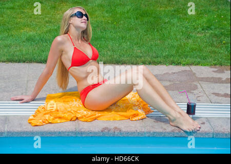 Young, attractive woman wearing a red bikini and sunbathing next to a swimming pool Stock Photo