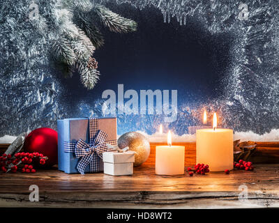 Gift boxes, candle lights and frozen window. Christmas background. Stock Photo