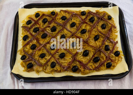 Anchovy lattice and olives on cooked onions on puff pastry when making pissaladiere, ready for cooking. Stock Photo