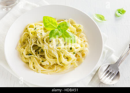 Tagliatelle pasta with pesto sauce, cheese and basil leaves on white plate close up - healthy homemade pasta Stock Photo