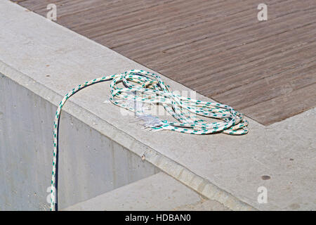 Coiled mooring line tied around cleat on a wooden dock. Stock Photo