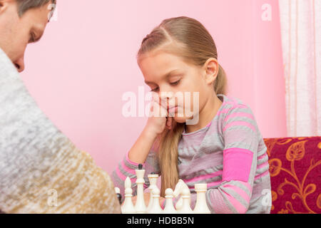 Seven-year daughter is thinking about the next move, playing chess Stock Photo