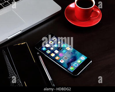 Apple iPhone 7 Plus on a desk with a cup of coffee, a Macbook laptop computer, and a notebook, on dark background Stock Photo