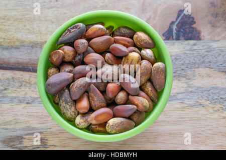 Unshelled pine nuts in a green bowl on aged wooden table, viewed from above Stock Photo