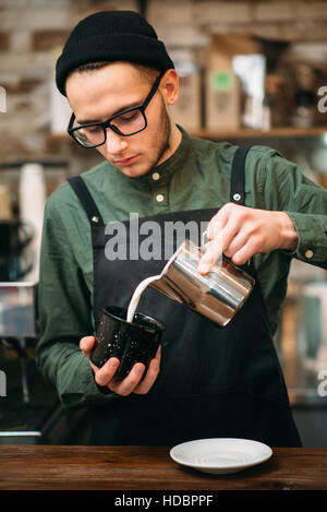 Waiter in black hat fill in a cup of milk, blur background. Stock Photo