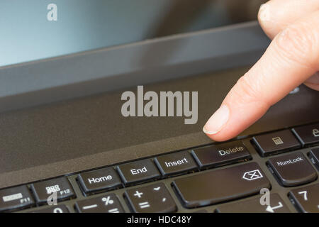 Women finger is ready to press the Delete key on the keyboard of a laptop. Stock Photo