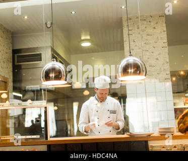 Young chef with white uniform standing at a modern kitchen in the restaurant and preparing food Stock Photo