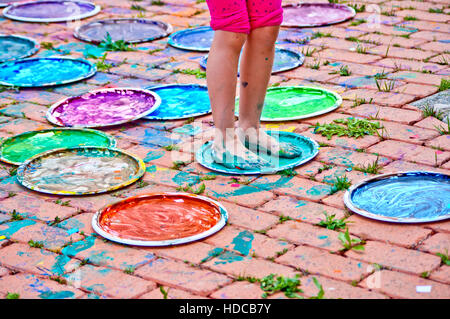 children playing making colorful designs with their feet immersed in the colorful tempera Stock Photo