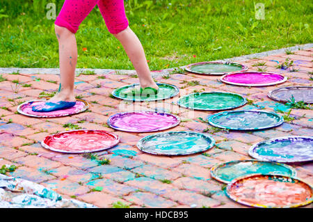 children playing making colorful designs with their feet immersed in the colorful tempera Stock Photo