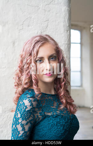 Beautiful young woman with pink hair wearing a green lace dress smiling indoors Stock Photo