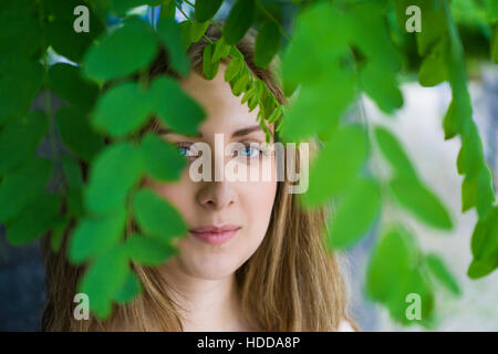 Beautiful young woman looking through the leaves outdoors Stock Photo