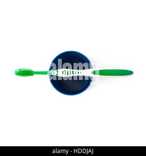 Green toothbrush with paste lying on blue plastic cup isolated over white background Stock Photo